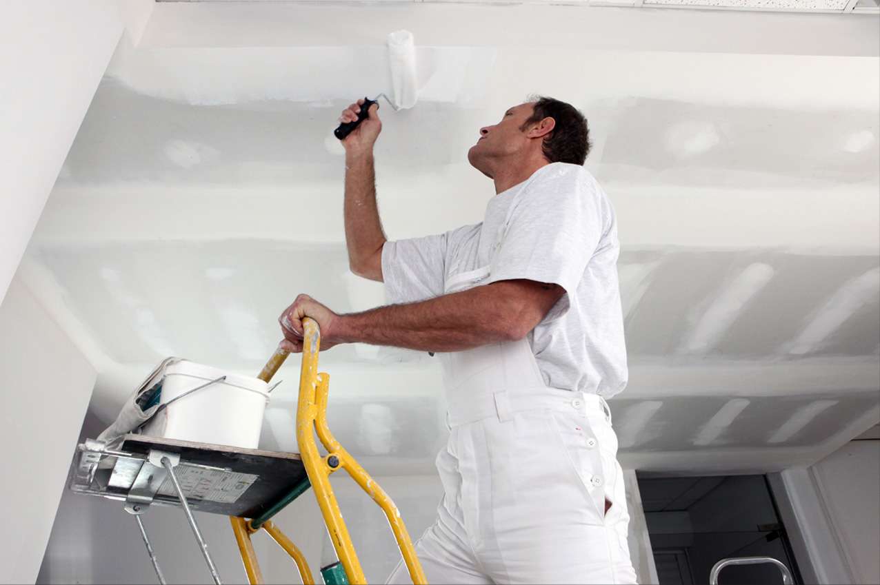 Painter in white overalls rolling paint onto a ceiling